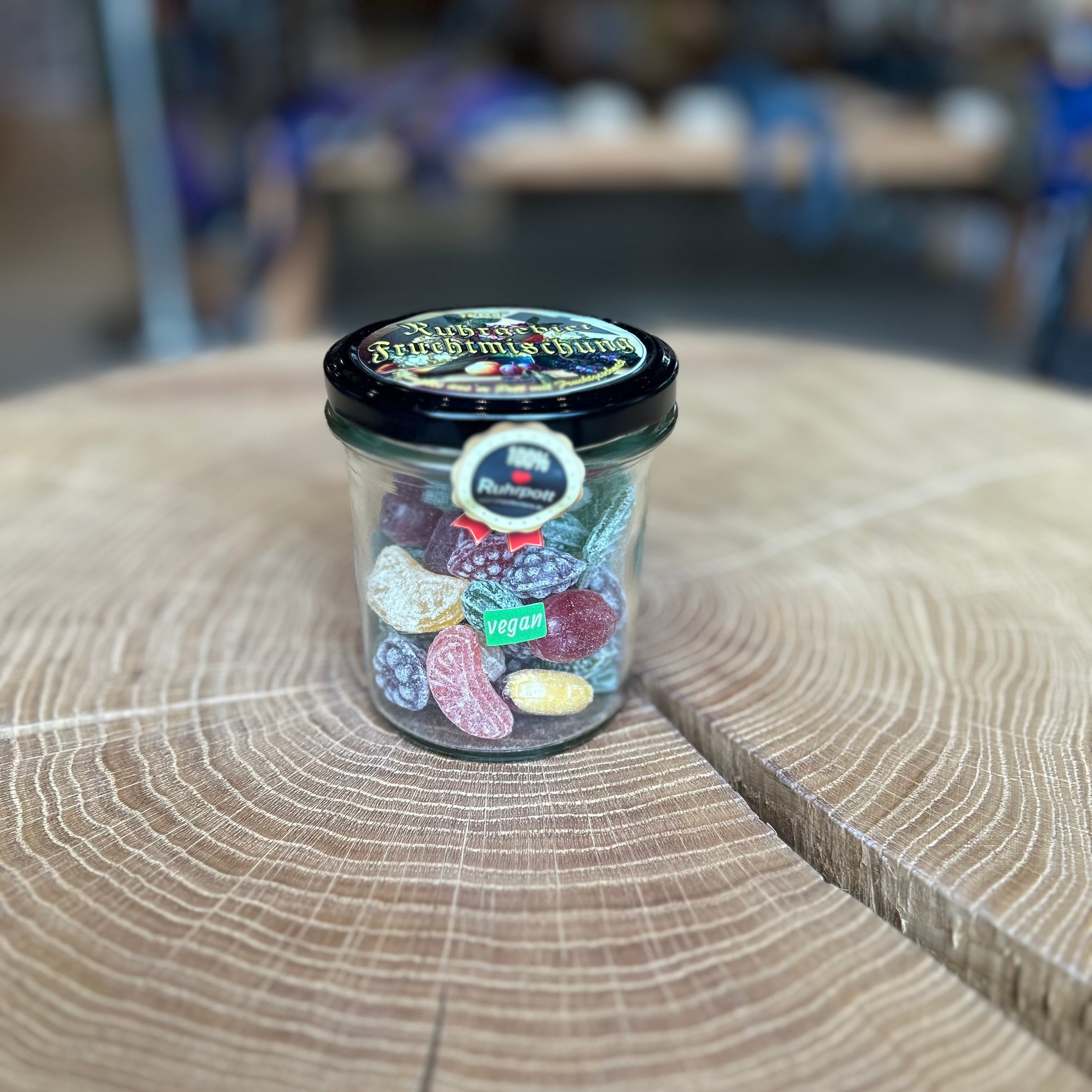 Glas mit bunter Bonbon Fruchtmischung – vegane Ruhrpott-Süßigkeit in verschiedenen Fruchtsorten, originelle Geschenkidee oder Souvenir aus dem Ruhrgebiet, präsentiert auf Holztisch.