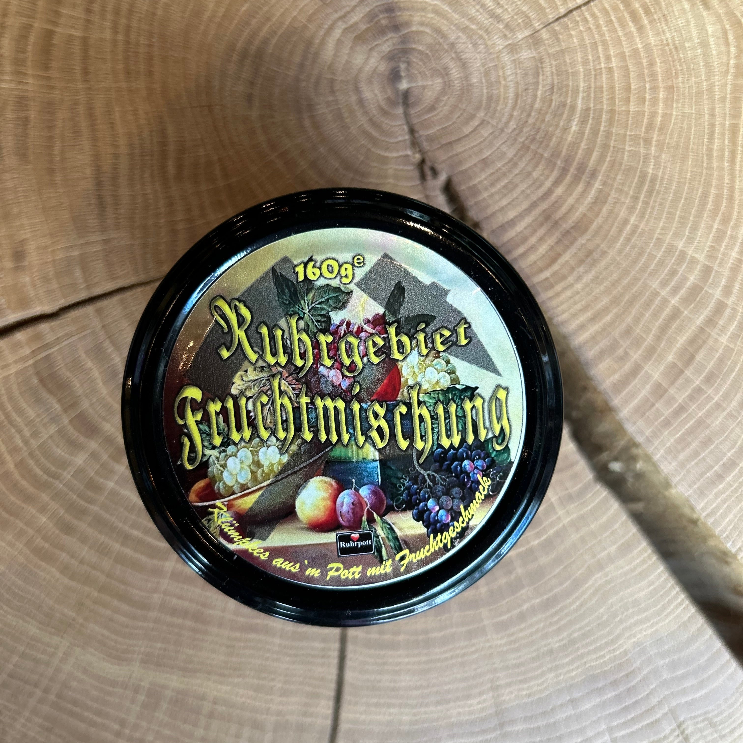 Glas mit bunter Bonbon Fruchtmischung , davon die der Deckel– vegane Ruhrpott-Süßigkeit in verschiedenen Fruchtsorten, originelle Geschenkidee oder Souvenir aus dem Ruhrgebiet, präsentiert auf Holztisch.