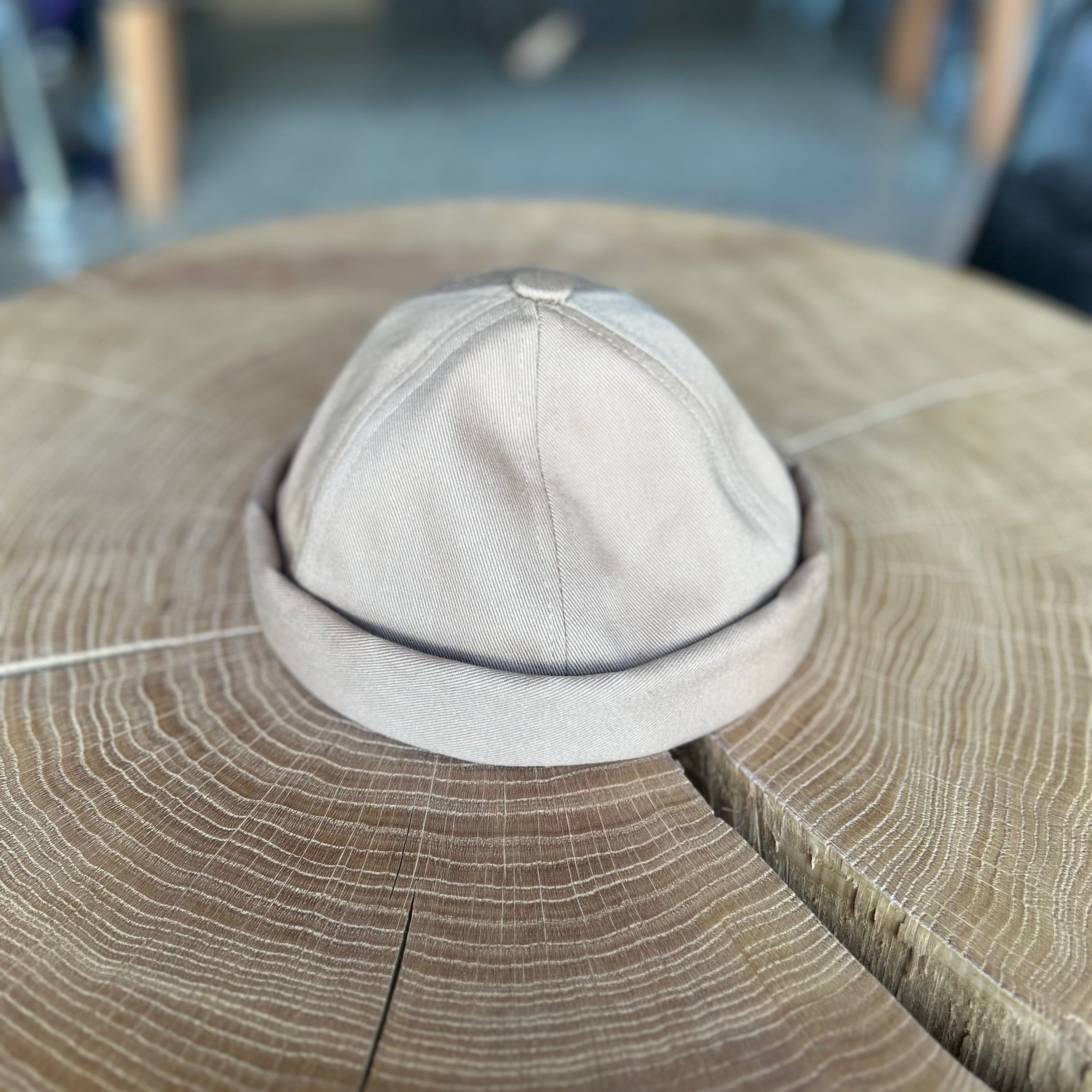 Fischermütze in der Farbe Beige, liegt auf einem Holztisch