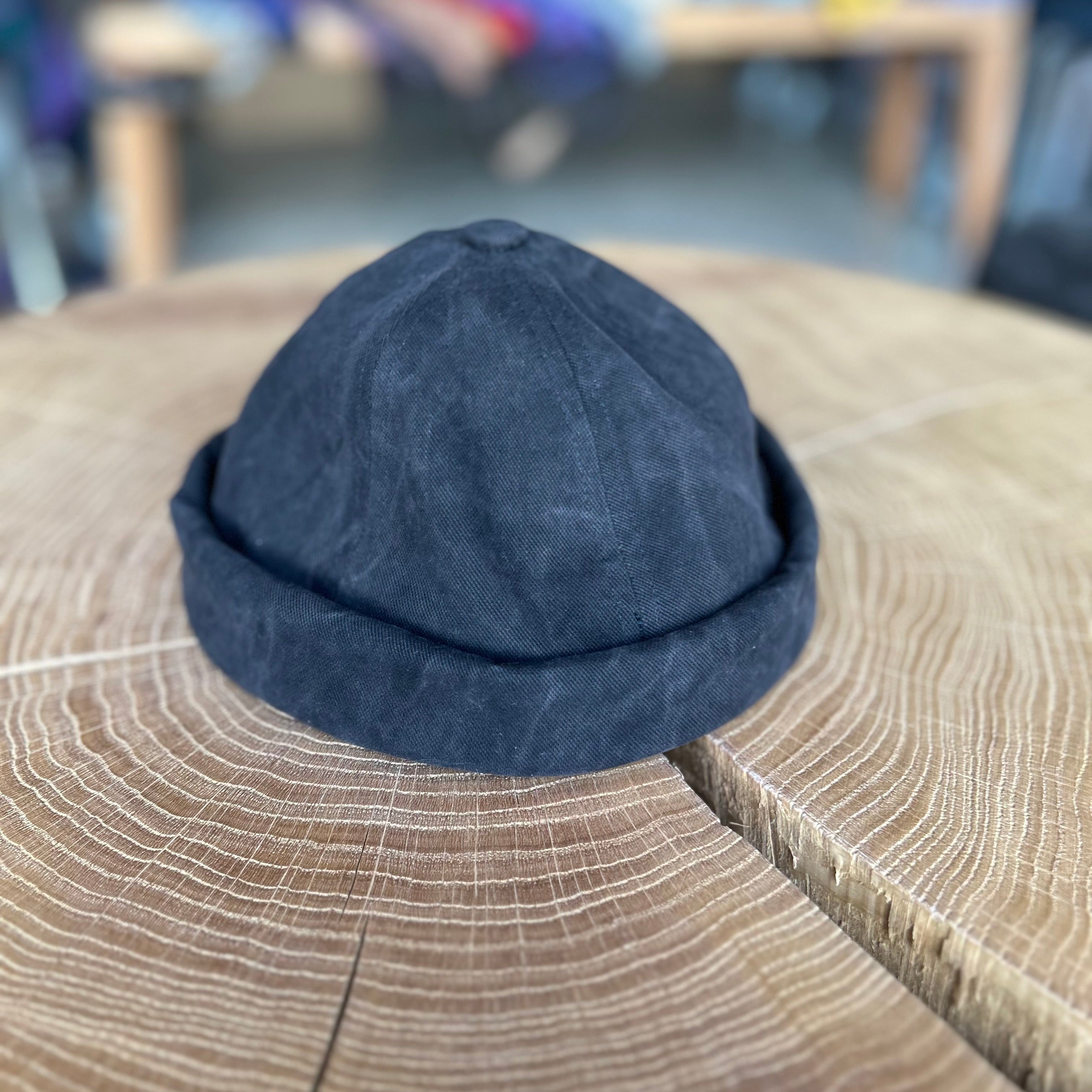 Fischermütze in der Farbe Grau, liegt auf einem Holztisch