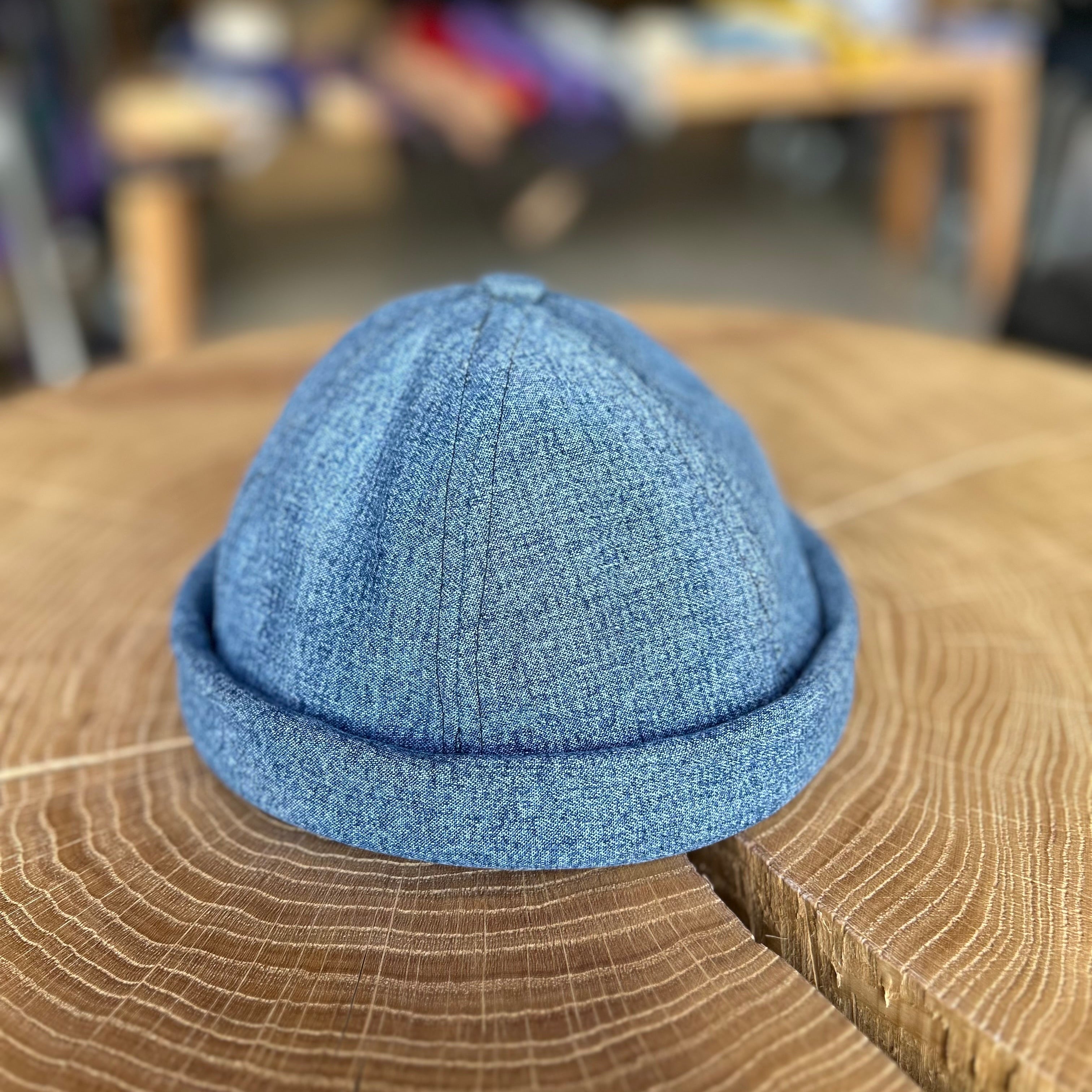Fischermütze in der Farbe Hell Jeans, liegt auf einem Holztisch