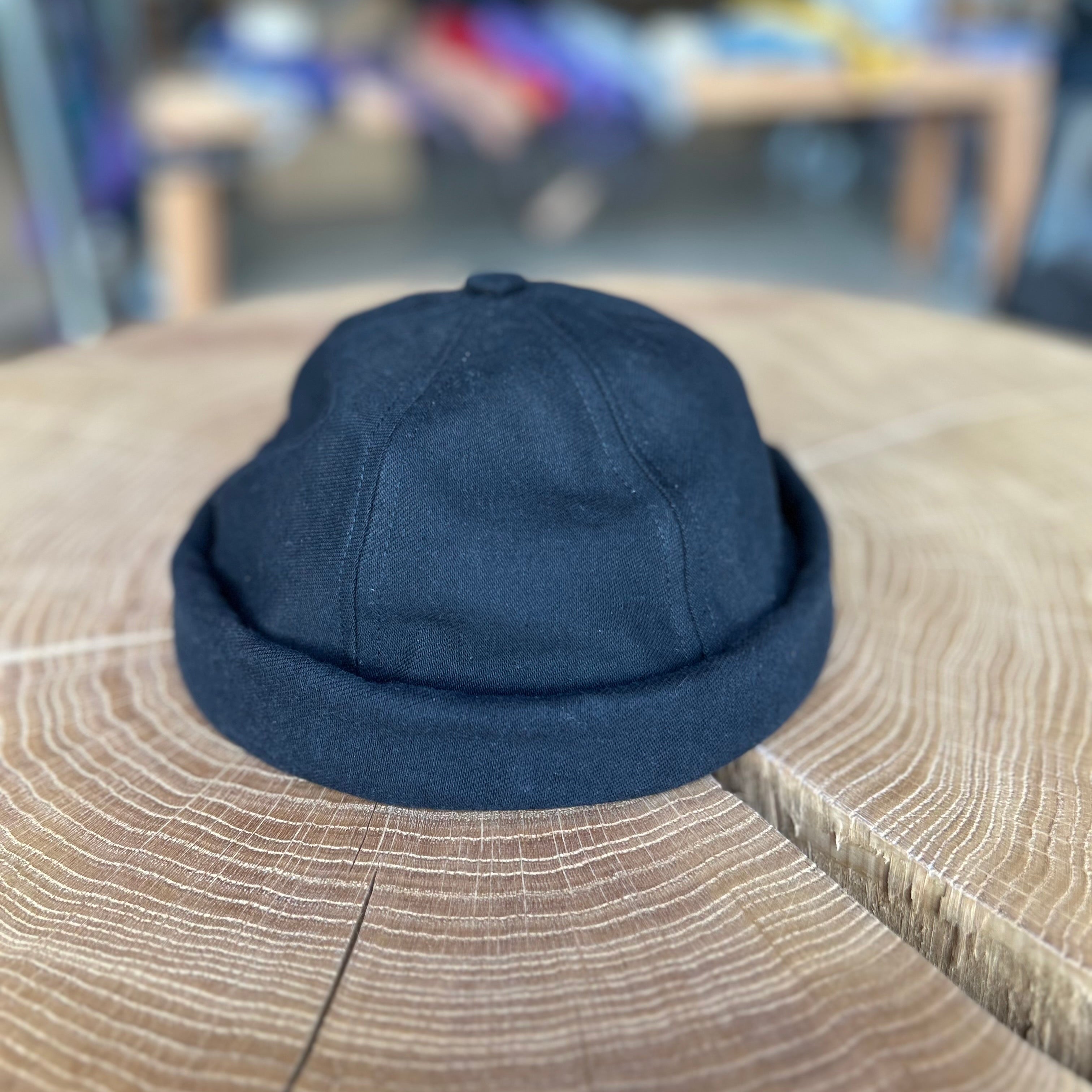 Fischermütze in der Farbe Schwarz, liegt auf einem Holztisch