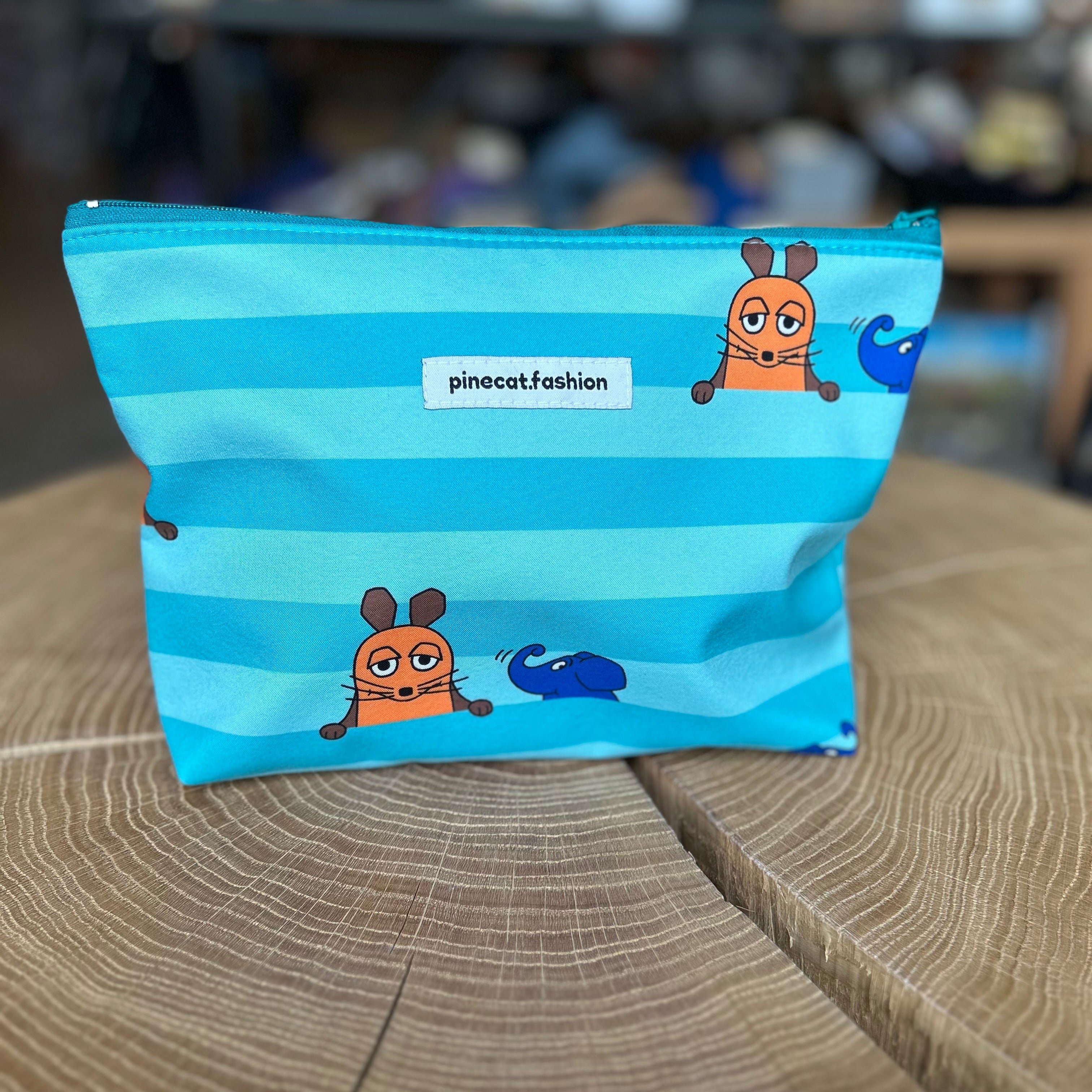 Große Kinder-Kosmetiktasche von Pinecat in Blau mit Streifen, verziert mit der Maus und dem Elefanten aus der Sendung mit der Maus, stehend auf einem Holztisch