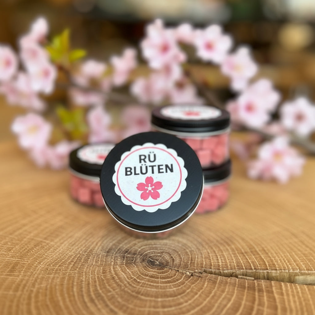 Kleine Dose mit rosa Seifenblüten „RÜ Blüten“ auf einem dekorativen Holztisch, im Hintergrund unscharfe Boutique-Atmosphäre. Handgemachte Mini-Seifenblüten als Geschenk, Dekoration oder Duftseife – ideal für Bad, Gäste-WC oder als Rüttenscheid-Souvenir.