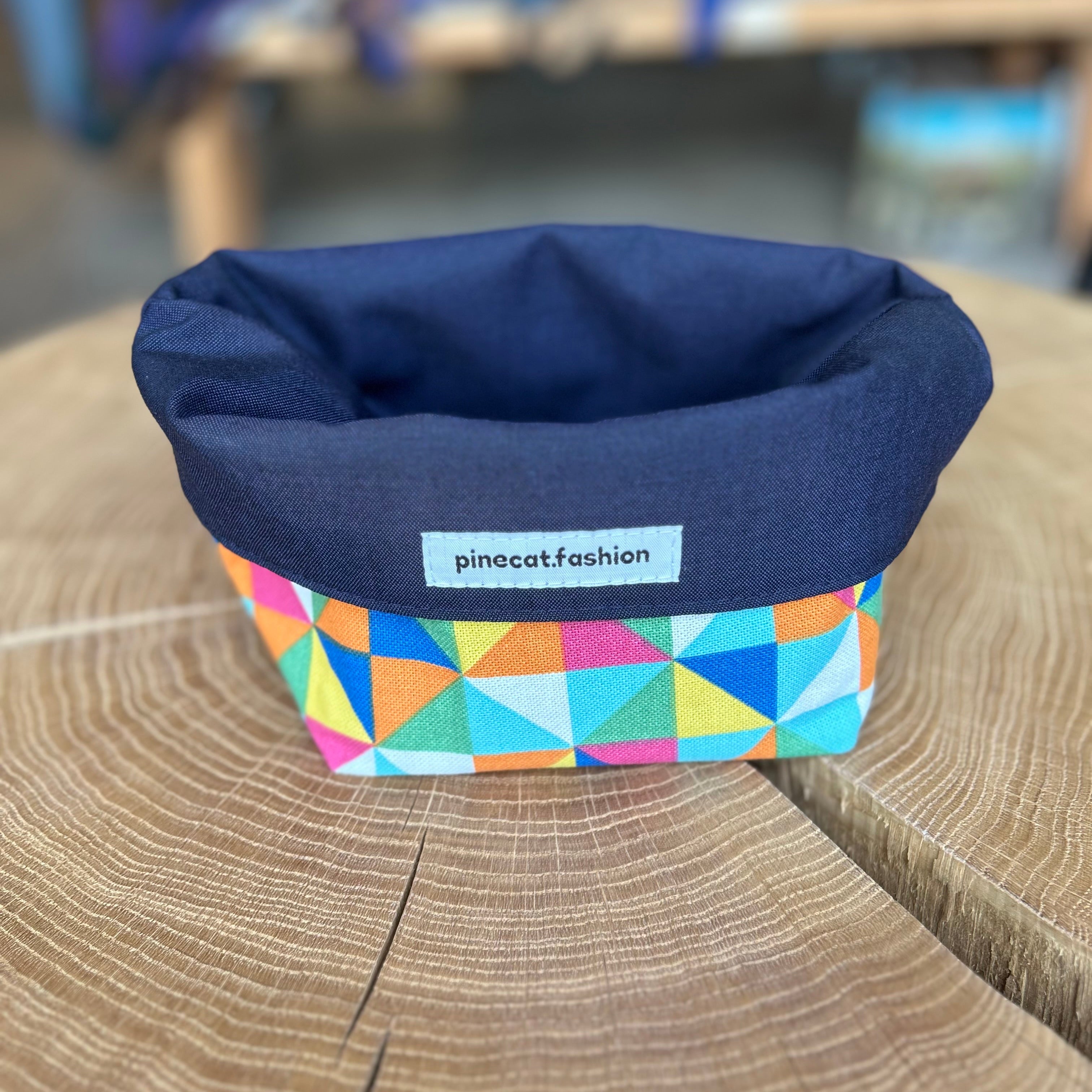 Pinecat Körbchen Blau-Bunt liegt auf einem Holztisch