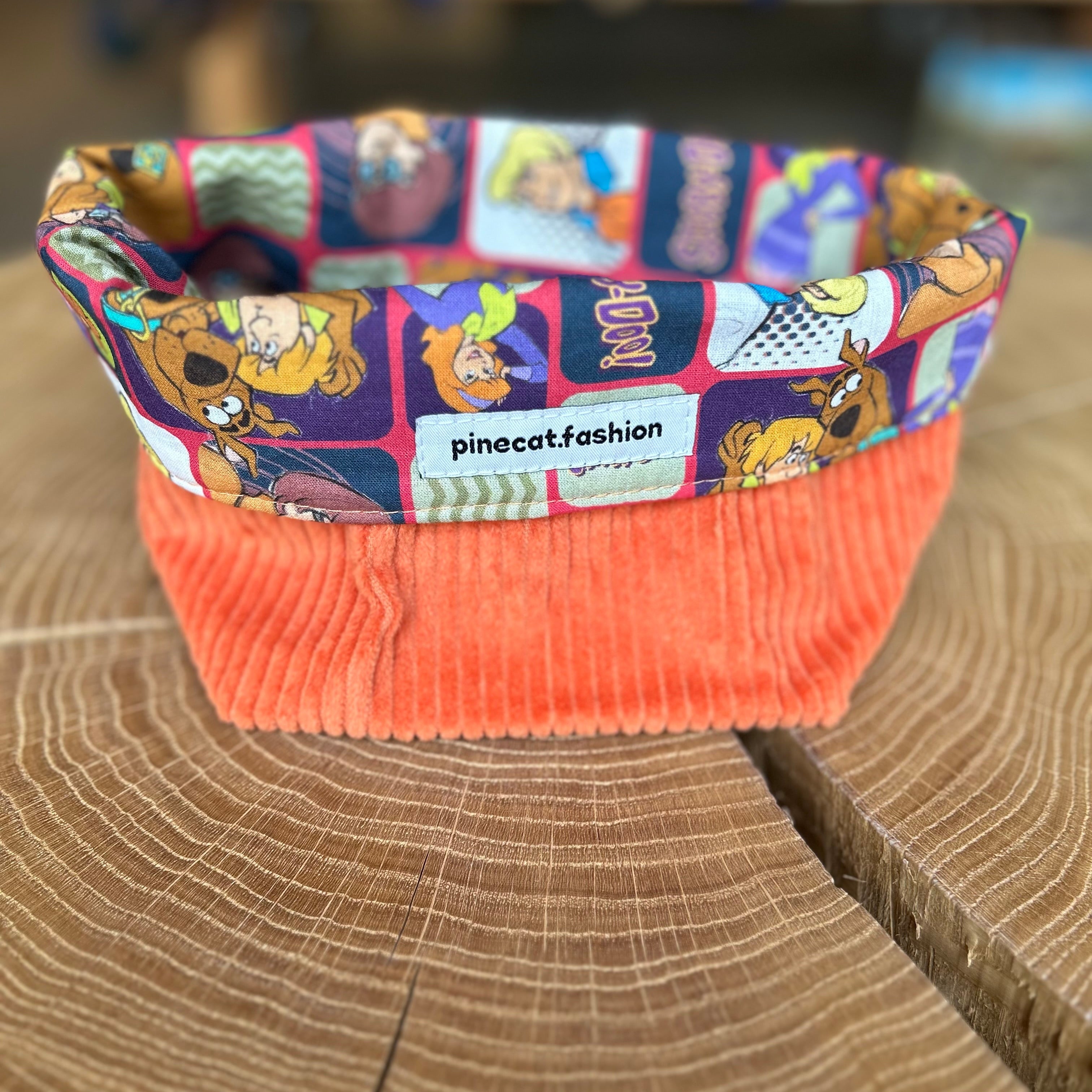 Pinecat Körbchen Orange liegt auf einem Holztisch