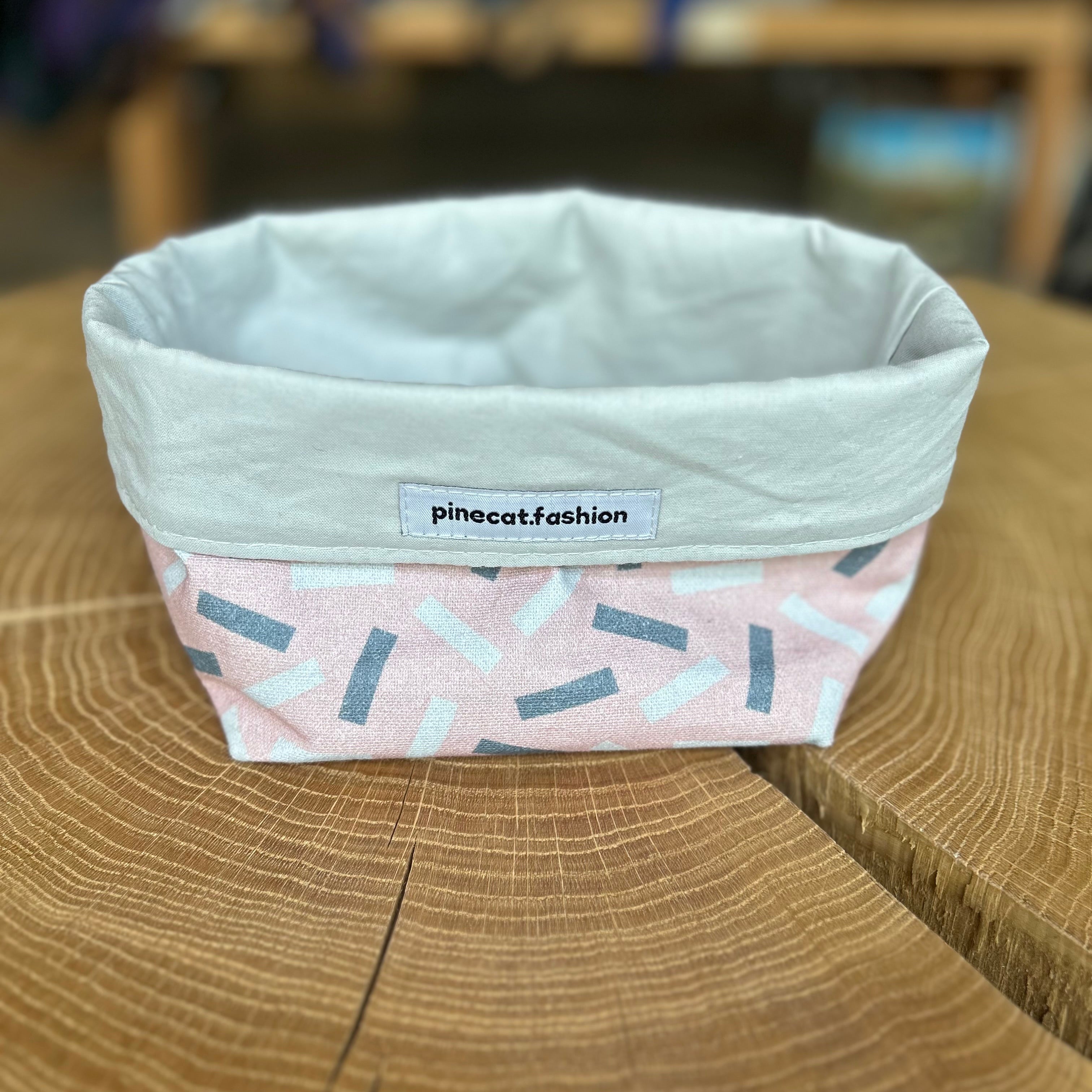 Pinecat Körbchen Rosa-Grau liegt auf einem Holztisch