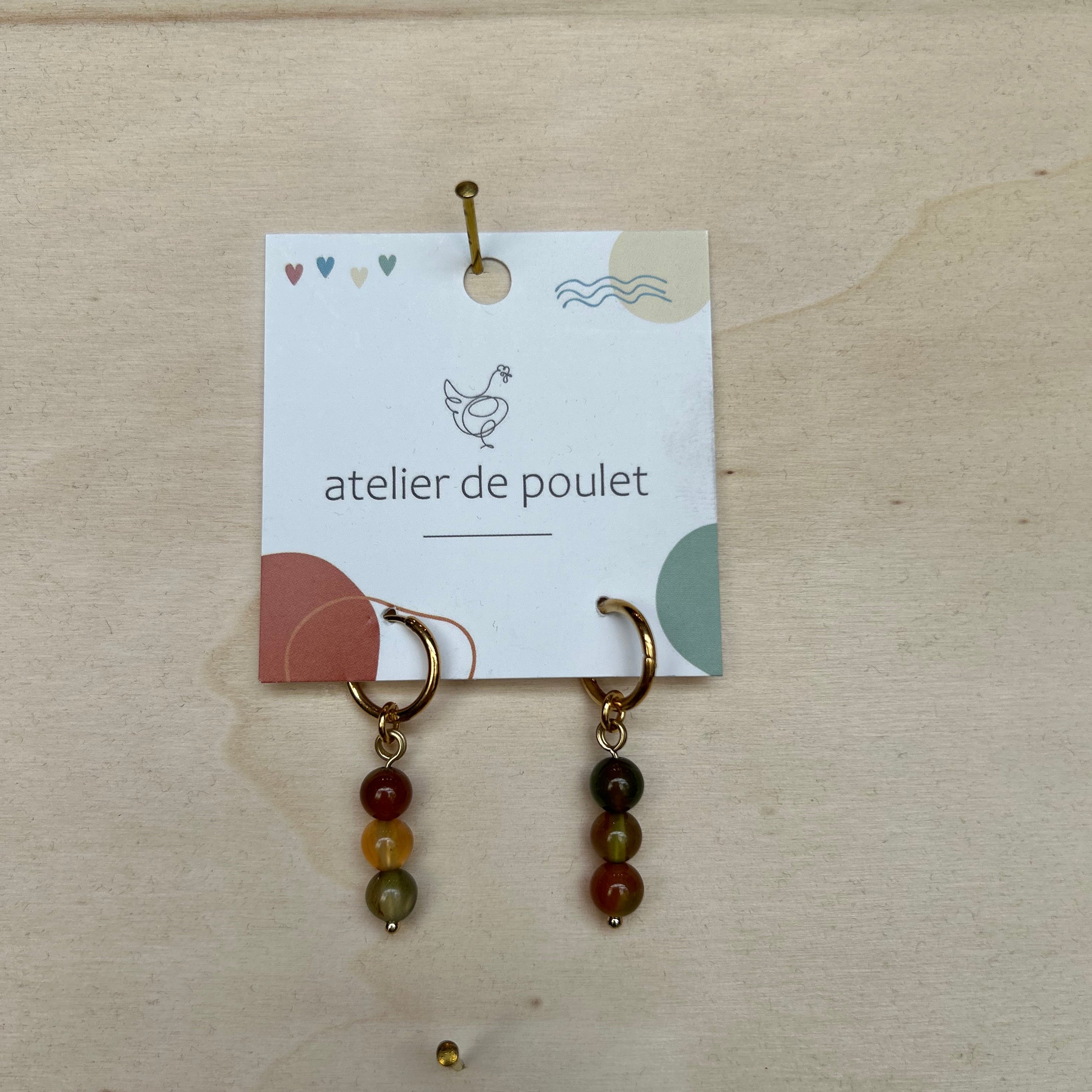 „Handgemachte Ohrringe von atelier de poulet – aus Edelsteinen in der Farbe Grün-Braun, präsentiert auf Holzdisplay. Stilvolle Damen-Ohrringe als individueller Modeschmuck, ideal als Geschenk oder Accessoire