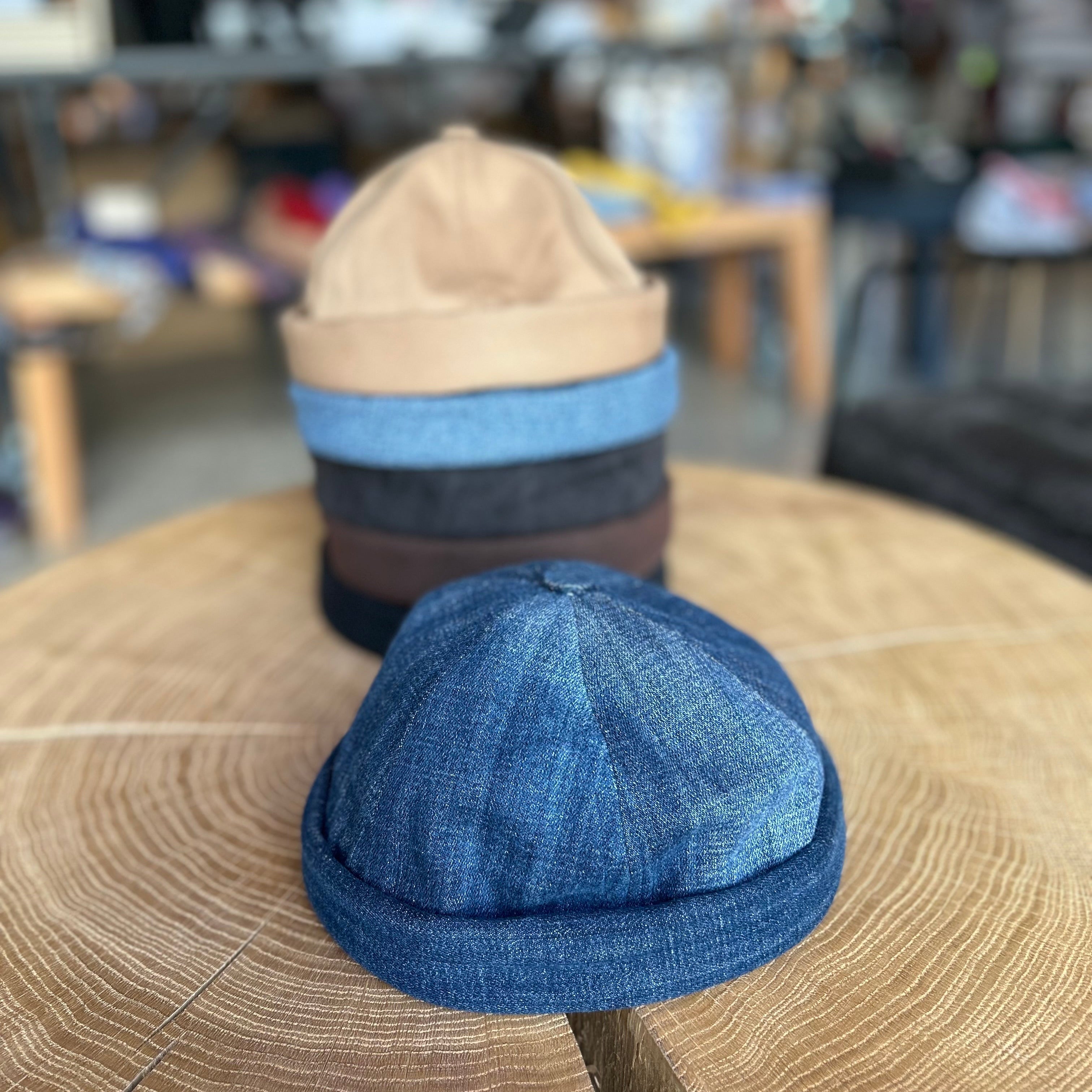 Sechs Fischermützen in der Farbe Dunkel Jeans, Hell Jeans, Beige, Grau, Schwarz. Alle Mützen liegen auf einem Holztisch