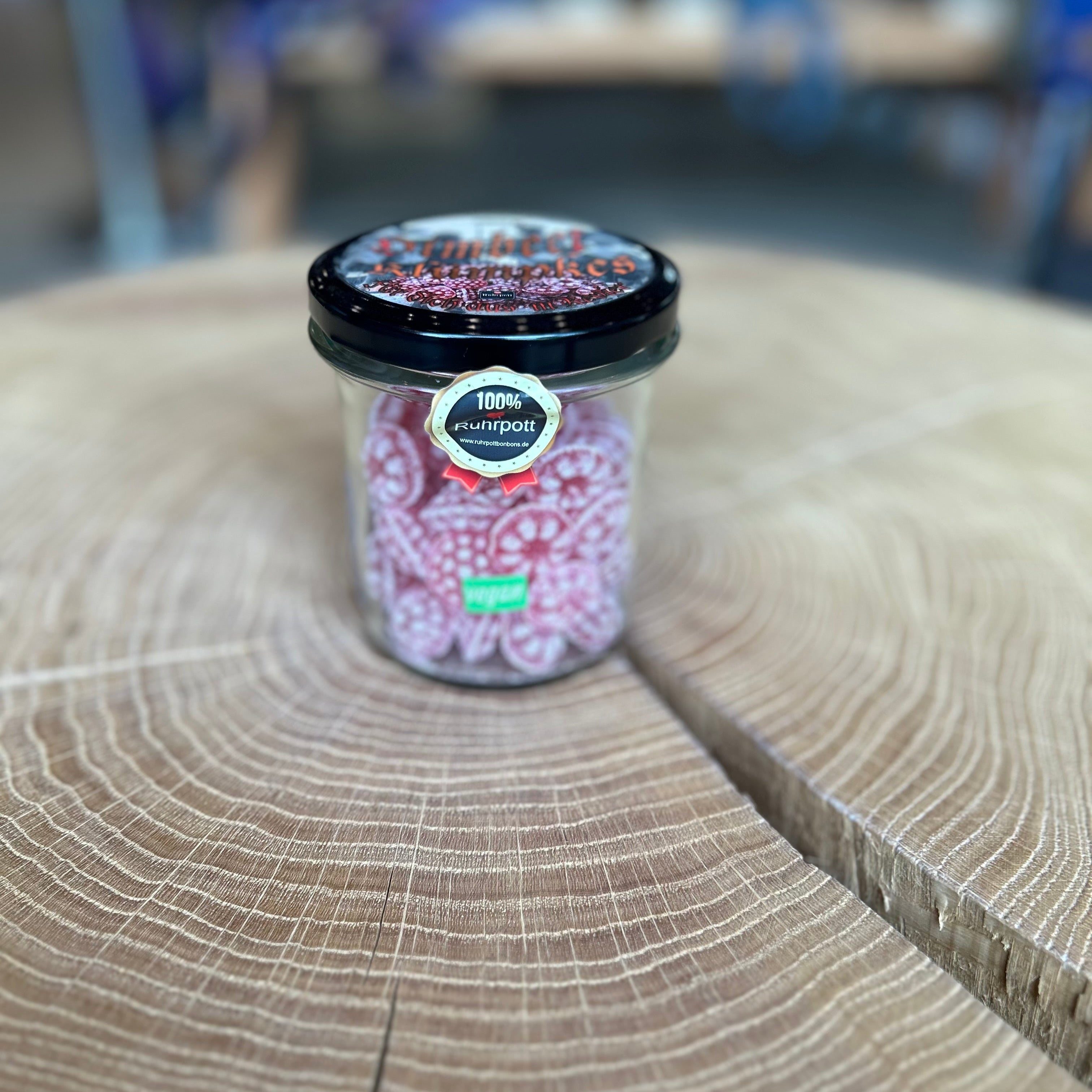 Glas mit Himbeer Bonbons – traditionelle rote Bonbons mit Himbeergeschmack, vegan und 100% Ruhrpott-Süßigkeit, ideale Geschenkidee oder Souvenir aus dem Ruhrgebiet, präsentiert auf Holztisch.