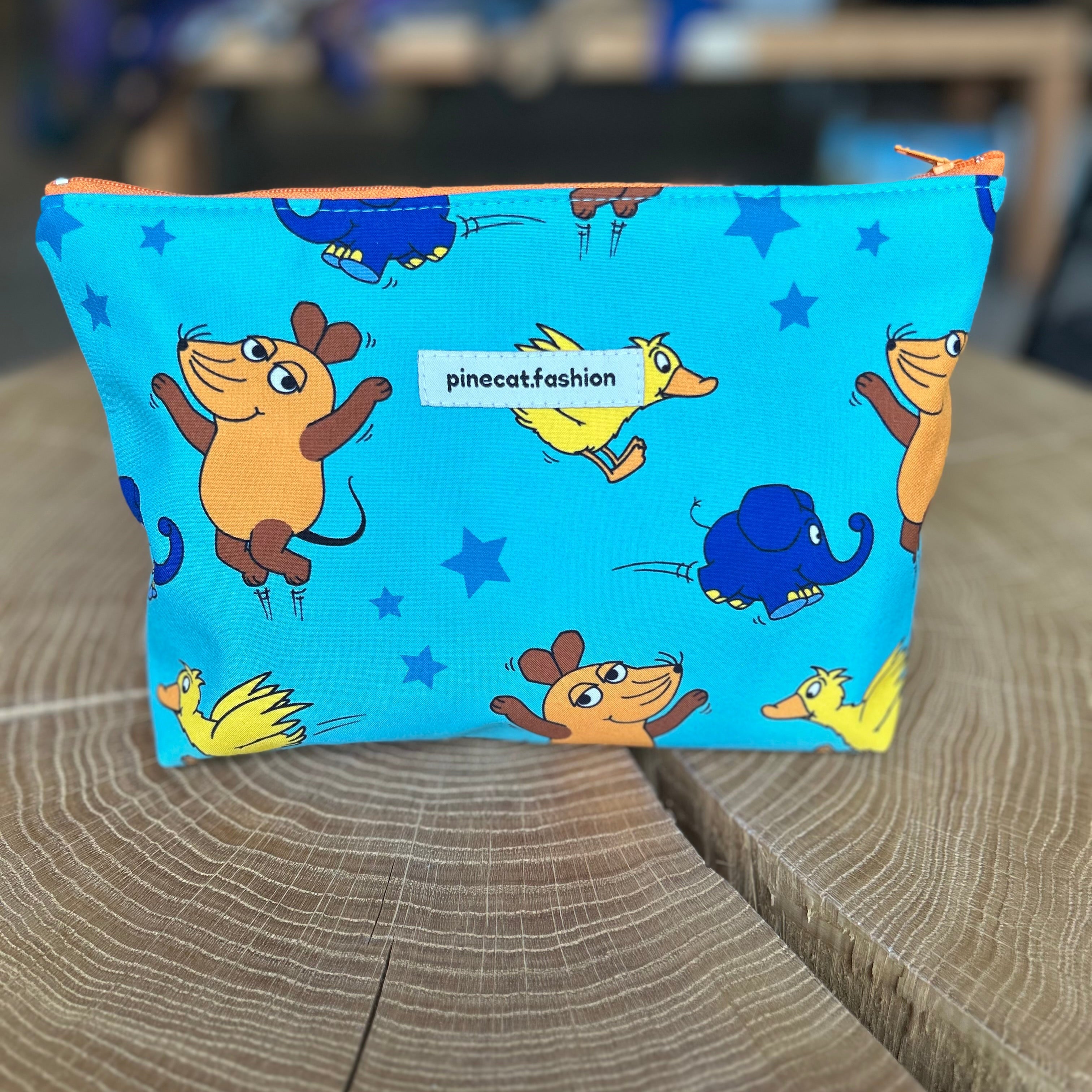 Große Kinder-Kosmetiktasche von Pinecat in Blau, verziert mit der Maus, der Ente und dem Elefanten aus der Sendung mit der Maus, stehend auf einem Holztisch