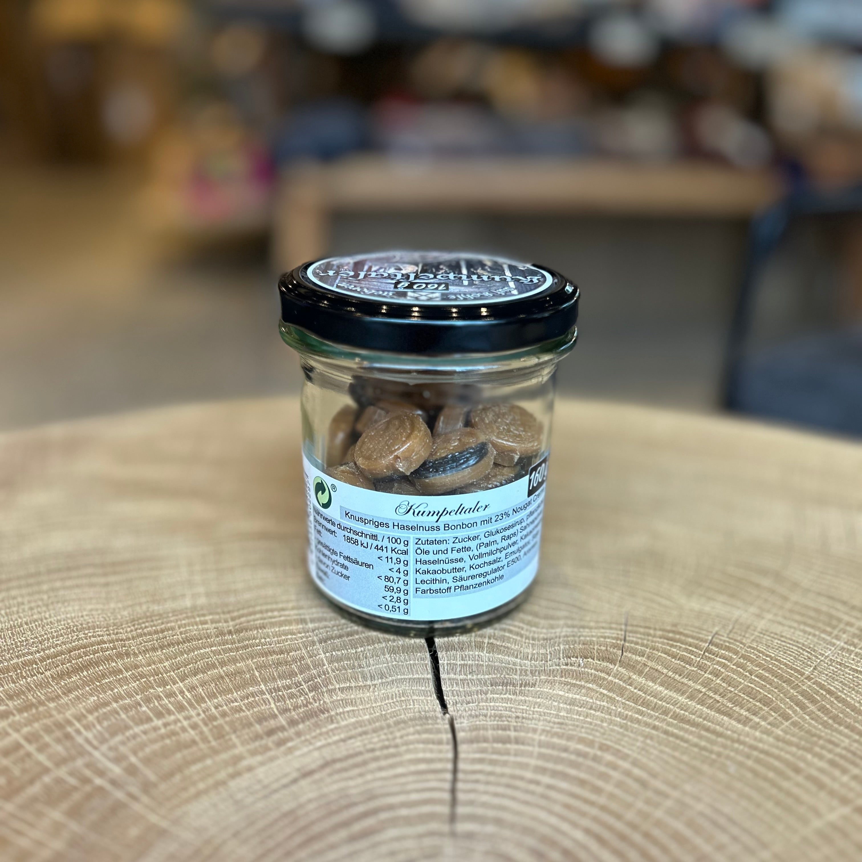 Glas mit braunen „Kumpeltaler Nougat Bonbons“ auf einem Holzuntergrund. Das Schraubglas ist gefüllt mit runden Nougatbonbons und trägt ein Etikett mit der Aufschrift „100% Ruhrpott“. Ideal als Geschenk oder regionales Mitbringsel aus dem Ruhrgebiet.