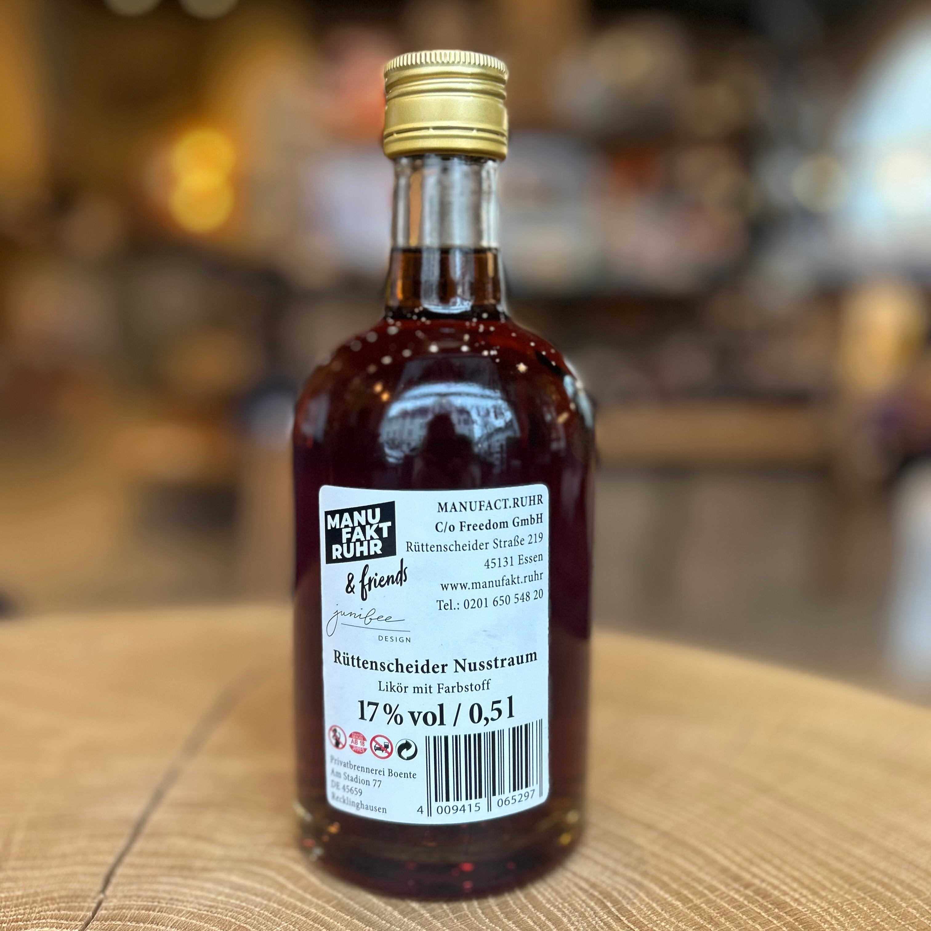 Flasche „Rüttenscheider Nuss Traum“ Likör (0,5 l, 17 % vol) auf einem Holztisch. Die braune Likörflasche trägt ein helles Etikett mit Haselnüssen und Blättern. Nuss-Nougat-Likör aus Essen-Rüttenscheid – ideal als Geschenk, Dessertlikör oder regionales Mitbringsel.