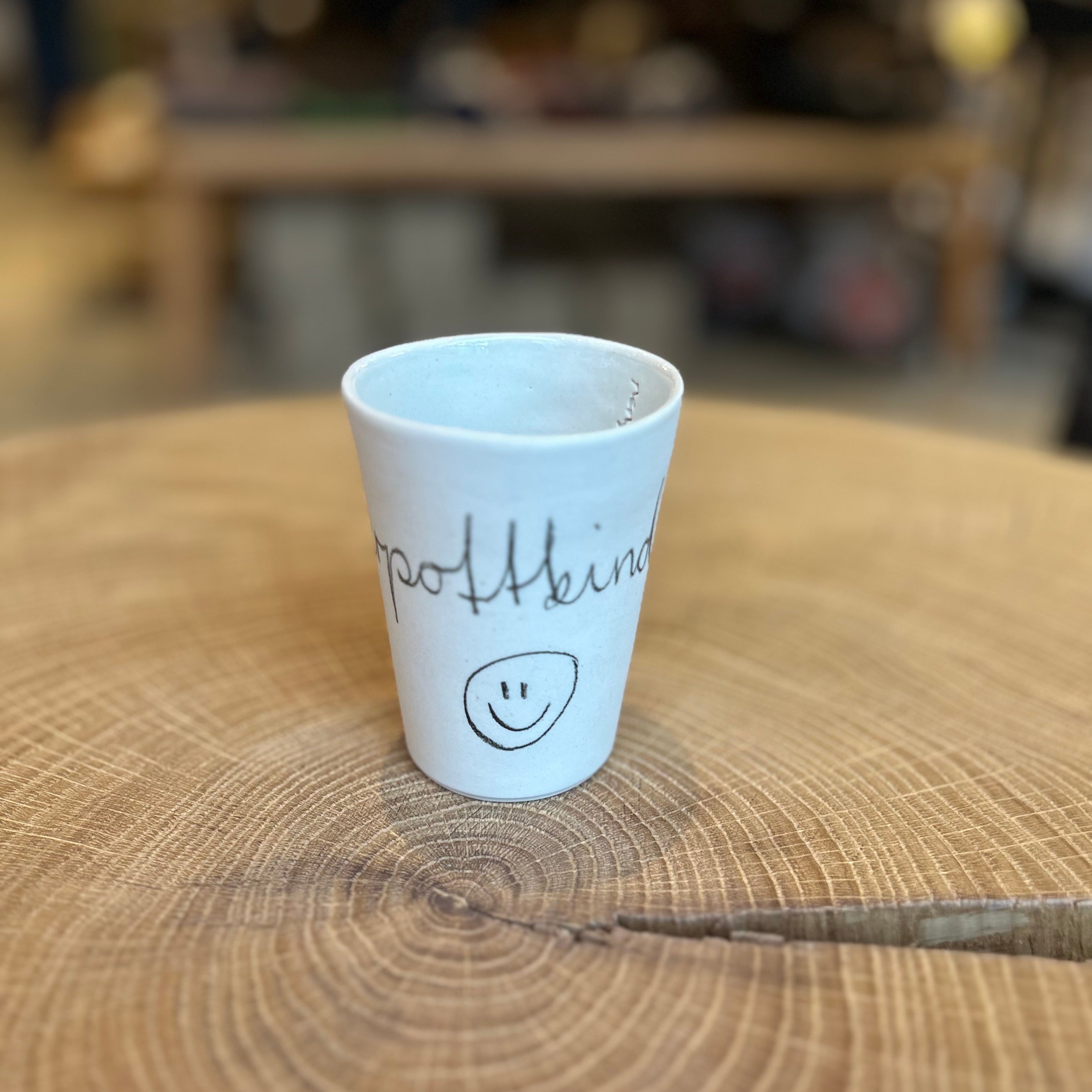  handgefertigte Keramikbecher in unterschiedlichen Größen mit der Aufschrift „Ruhrpottkind“ und Smiley, auf einer rustikalen Holzscheibe arrangiert – minimalistisches Design, regionale Keramik, Geschenkidee aus dem Ruhrgebiet.