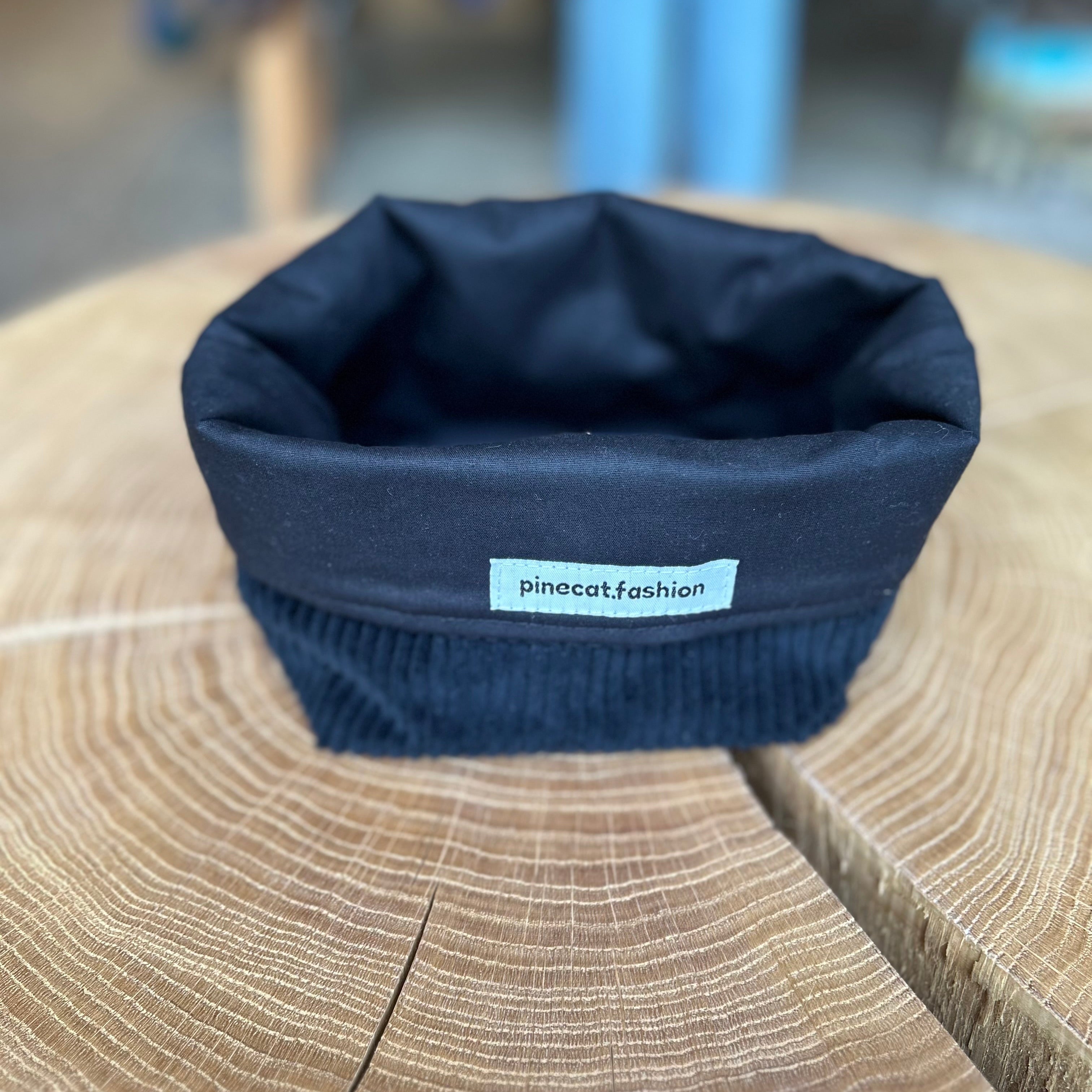 Pinecat Körbchen Schwarz liegt auf einem Holztisch