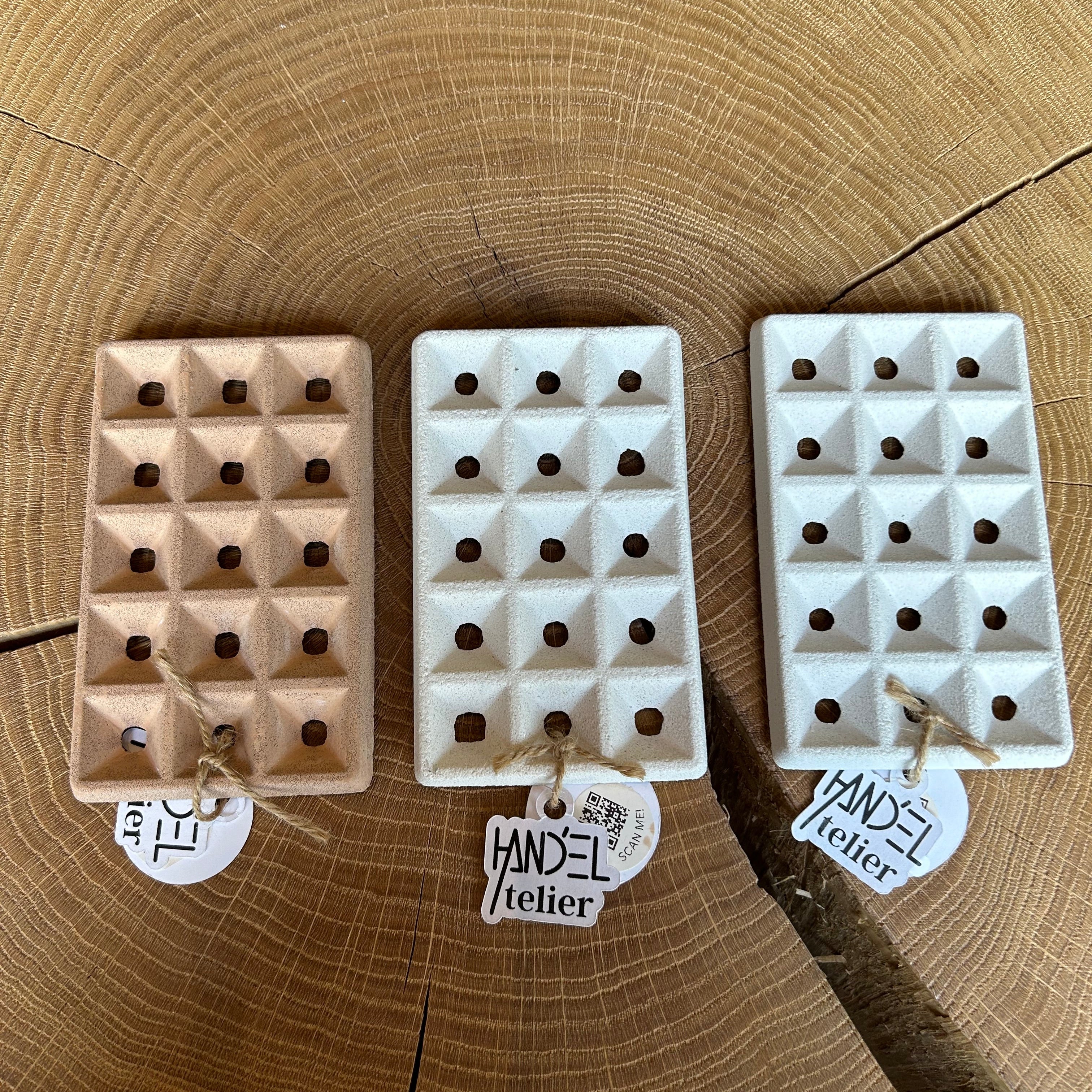Drei Seifenablagen aus Keramik in Beige und weiß, liegen auf einem Holztisch