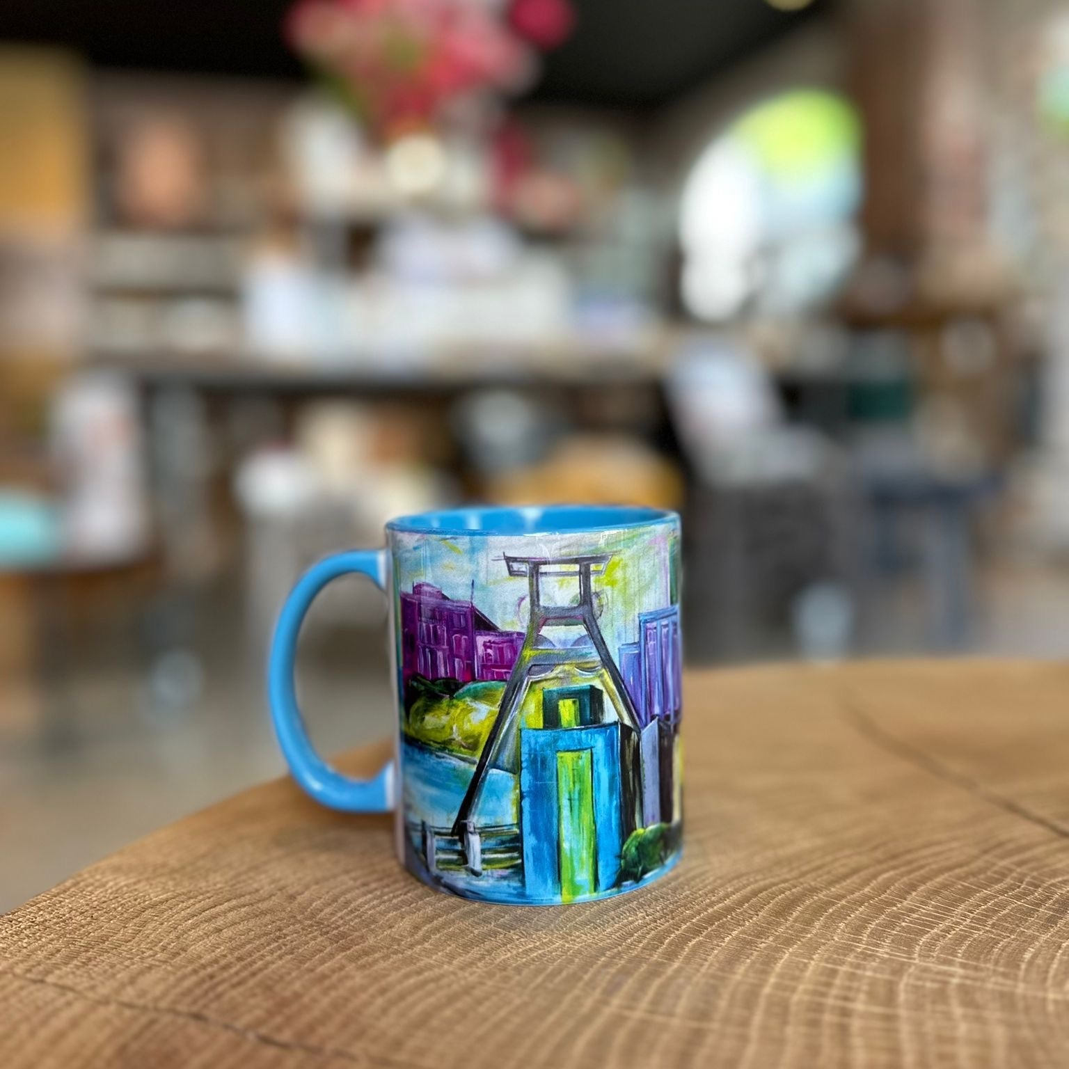 „Bunte Tasse mit Essen-Motiv aus dem Ruhrgebiet auf Holztisch – farbenfrohe Keramiktasse „Essen von Pott in Farbe“ mit Zeche und Skyline-Design im modernen Café.“
