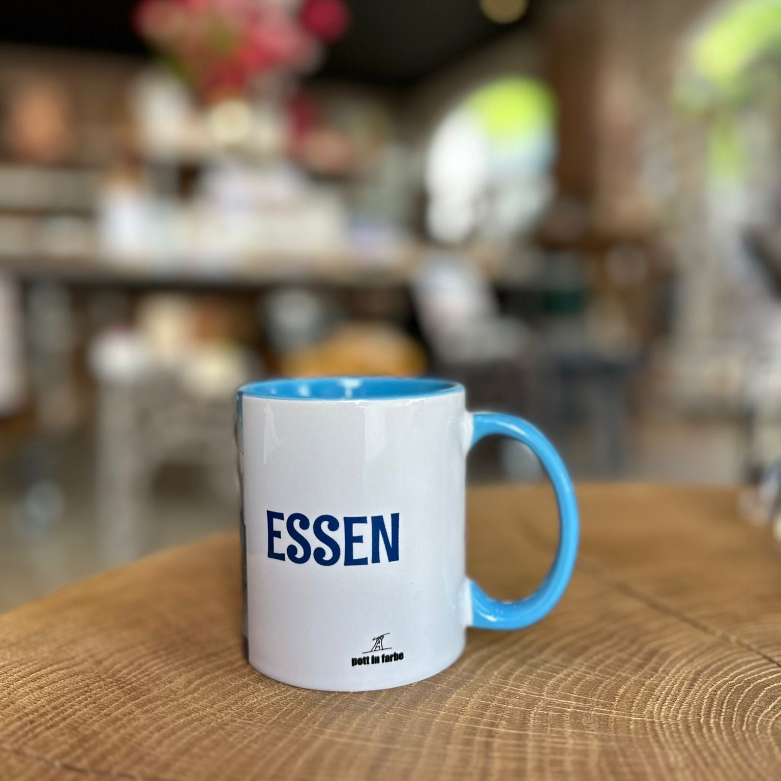 „Bunte Tasse mit Essen-Motiv aus dem Ruhrgebiet auf Holztisch – farbenfrohe Keramiktasse „Essen von Pott in Farbe“ mit Zeche und Skyline-Design im modernen Café.“